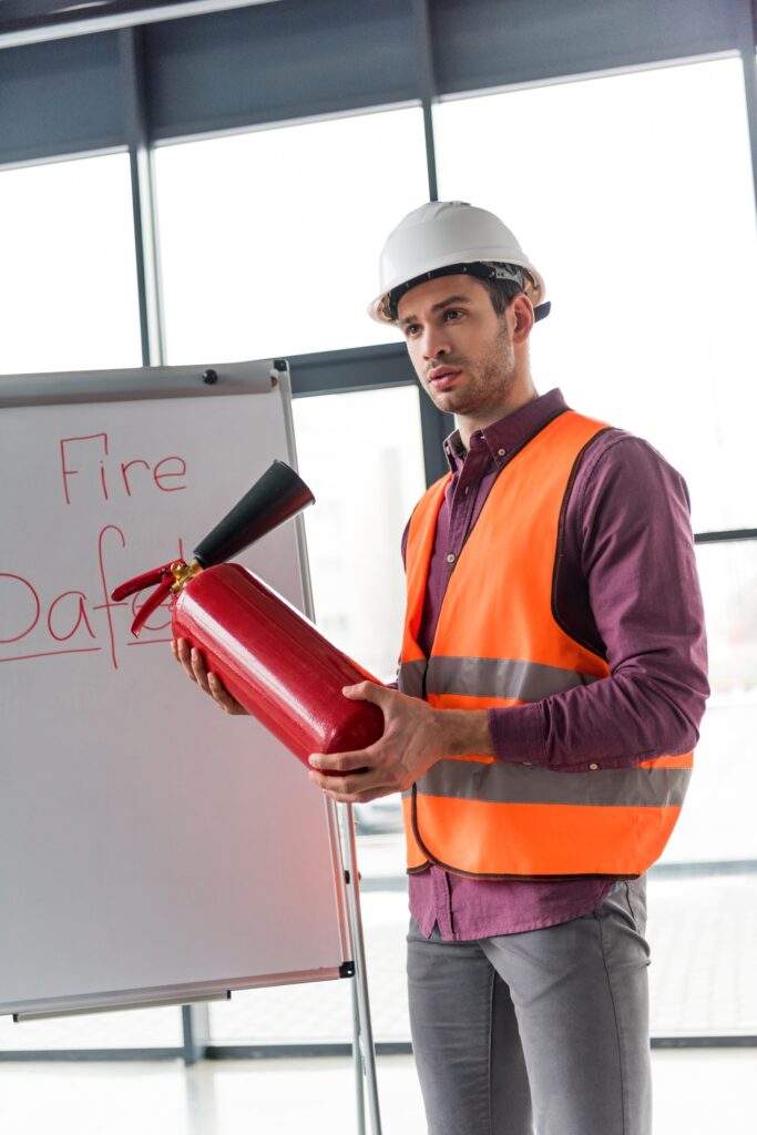 Qui sommes nous ? 2 handsome fireman holding red extinguisher and standing near white board with fire safety lettering